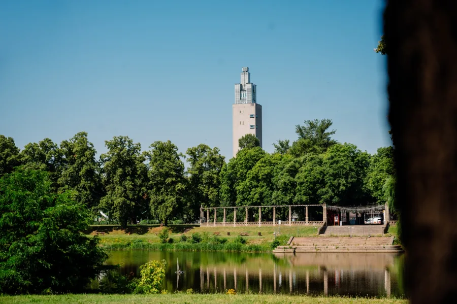 Der Albinm&uuml;ller-Turm &uuml;berragt die B&auml;ume am Adolf-Mittag-See, davor die Pergola am Ufer