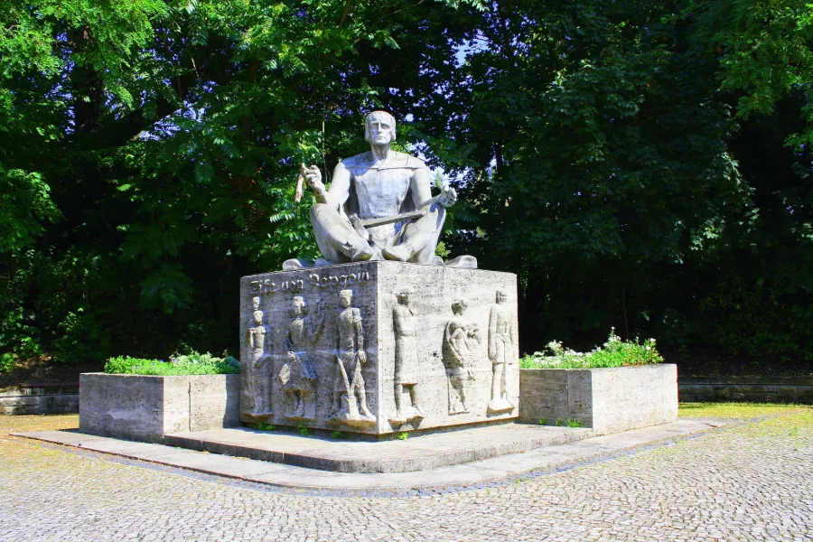 Steinernes Denkmal f&uuml;r Eike von Repgow: sitzende Figur auf einem Sockel mit Reliefs von Menschen