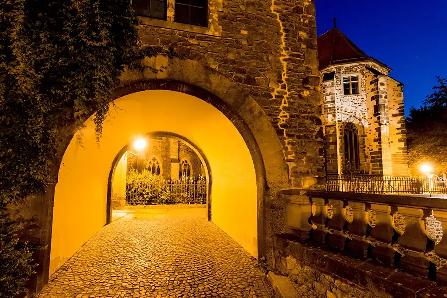 Der Remtergang bei Nacht: warm beleuchteter Torbogen mit Kopfsteinpflaster am Dom, rechts ein Wehrtuermchen mit Fachwerkerker und die Balustrade der Domterrasse
