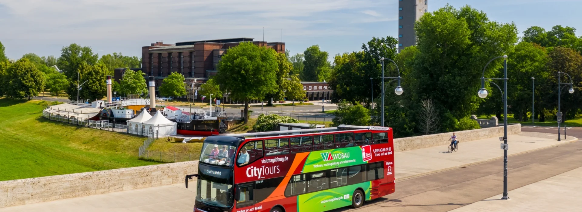 Der rote CityTours-Doppeldeckerbus mit offenem Oberdeck faehrt ueber die Strombruecke, dahinter Stadthalle und Albinmueller-Turm im Stadtpark