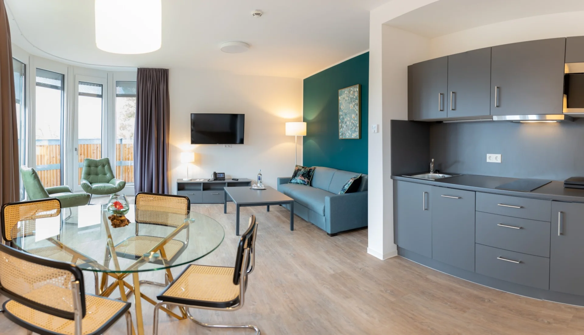 Panoramaaufnahme von Zimmer mit K&uuml;chennische, Essbereich und Sofaecke mit TV