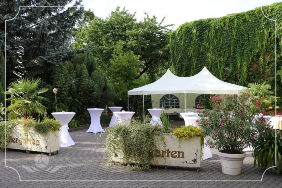 Hotelgarten mit wei&szlig;em Pagodenzelt, Stehtischen mit wei&szlig;en Hussen und bepflanzten K&uuml;beln vor einer dicht begr&uuml;nten Wand