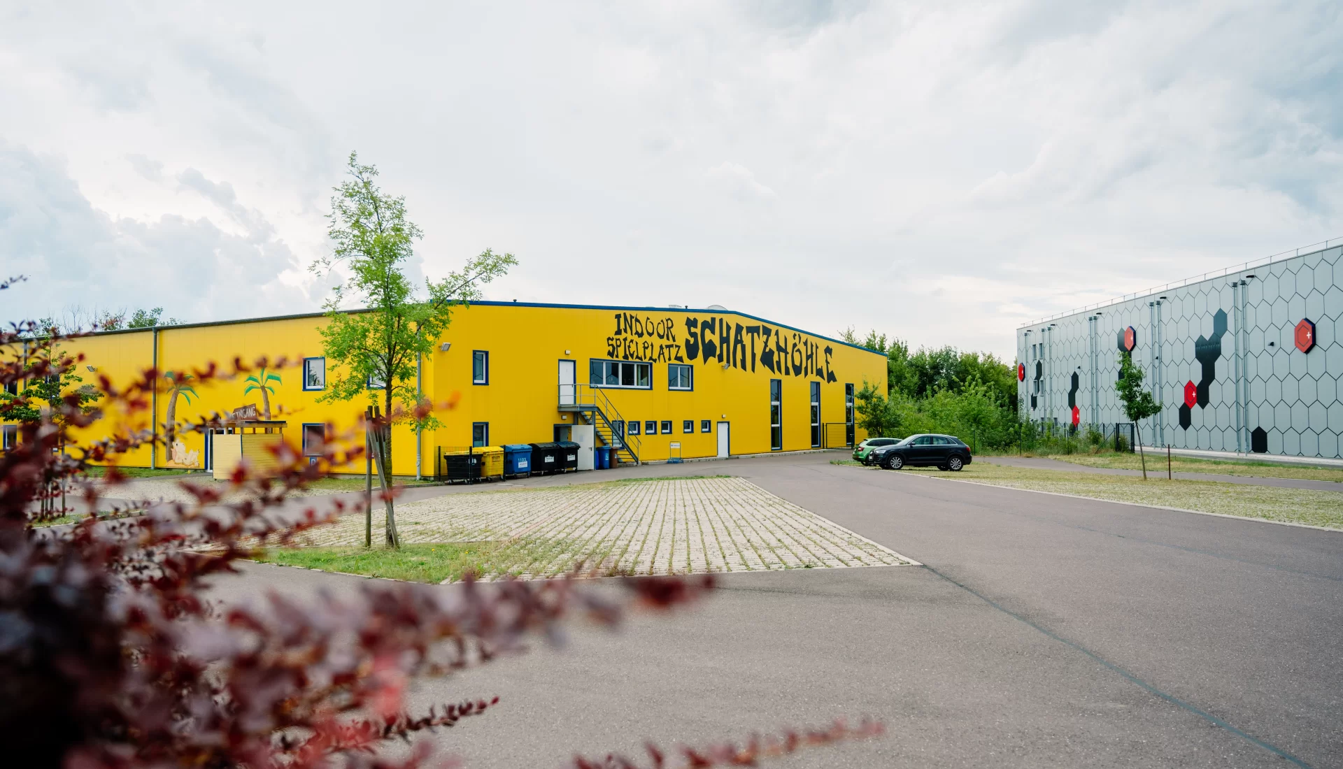 Au&szlig;enansicht der Schatzh&ouml;hle Magdeburg mit gro&szlig;em Parkplatz. Im Vordergrund ein Busch.