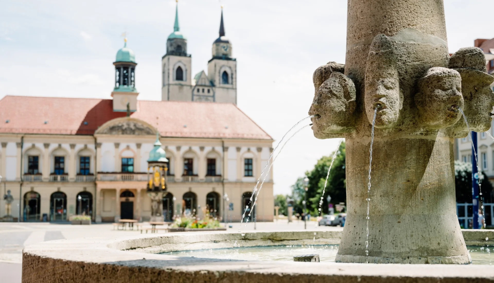 Wasserspeiende Steink&ouml;pfe am Brunnen auf dem Rathausplatz, dahinter unscharf das Magdeburger Rathaus und die Johanniskirche