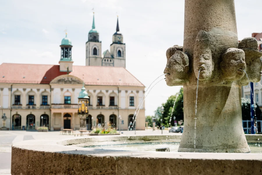 Wasserspeiende Steink&ouml;pfe am Brunnen auf dem Rathausplatz, dahinter unscharf das Magdeburger Rathaus und die Johanniskirche