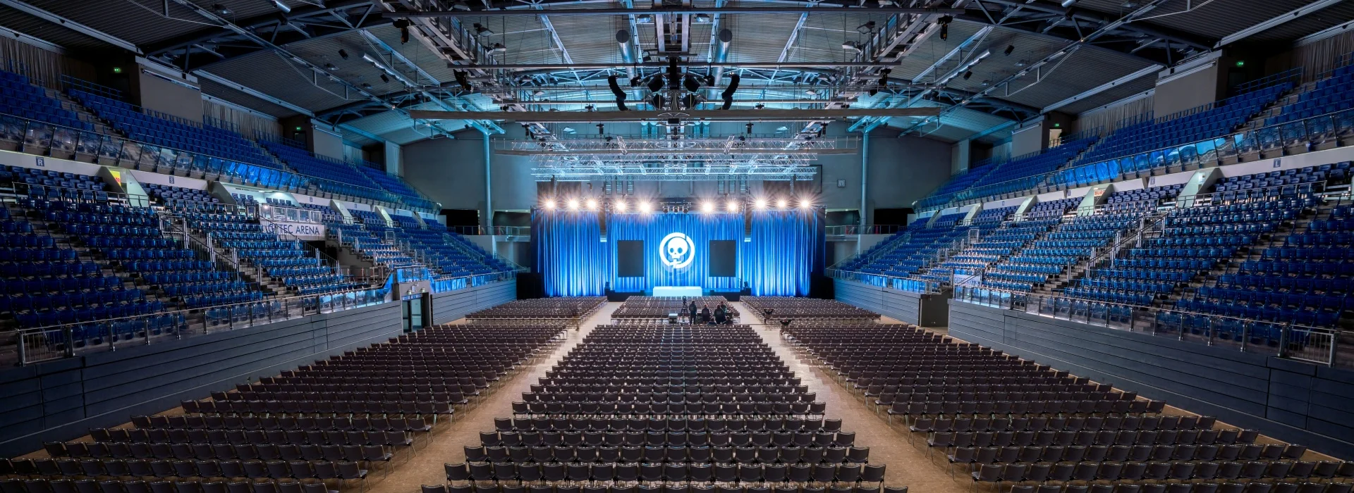 Innenraum der Avnet Arena Magdeburg in gro&szlig;er Kongressbestuhlung: hunderte Stuhlreihen vor einer blau ausgeleuchteten B&uuml;hne, ringsum leere blaue Trib&uuml;nenr&auml;nge