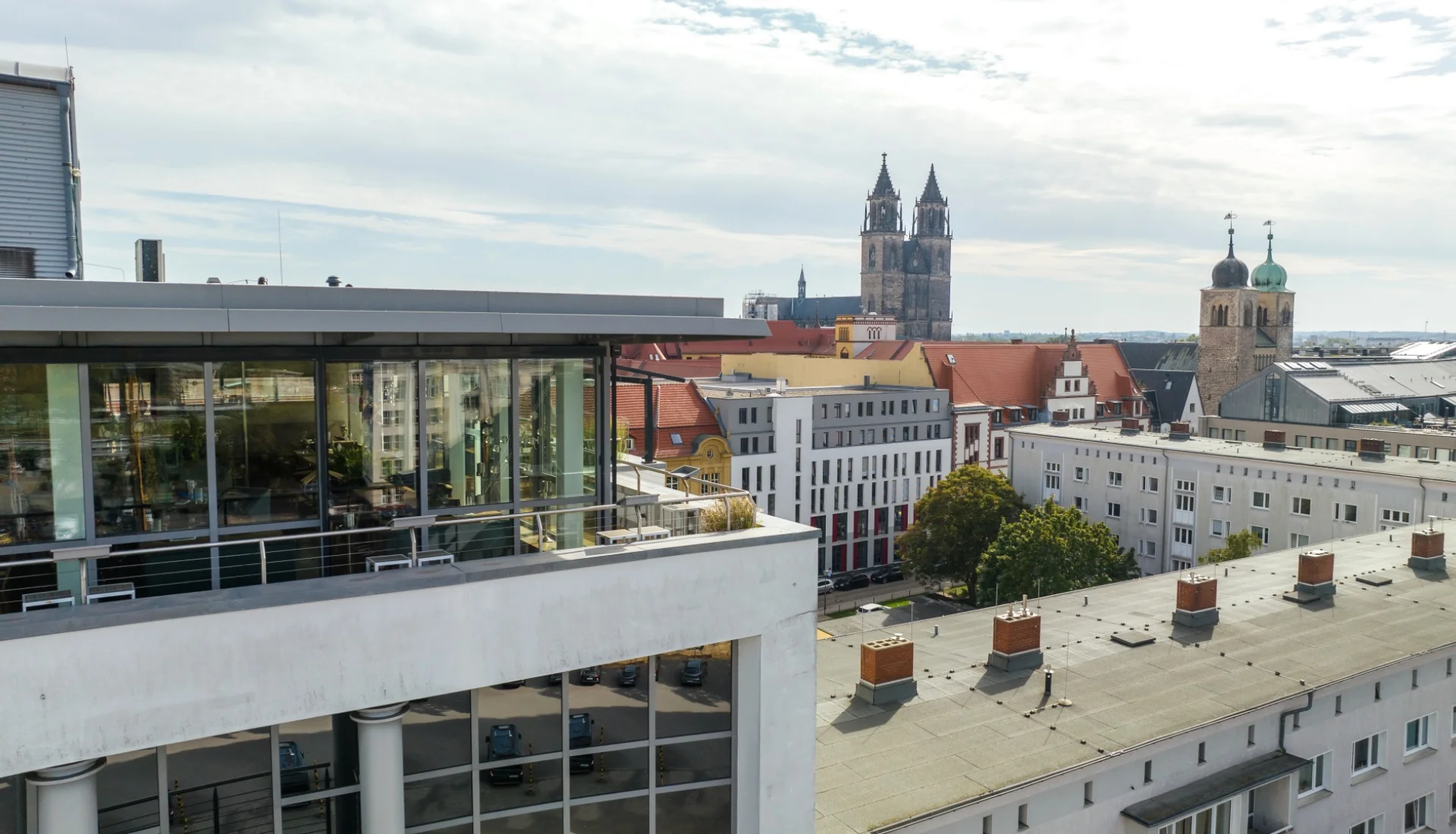 Blick von der Dachterrasse der Rooftop-Bar The Bird ueber die Daecher der Magdeburger Altstadt, links der verglaste Barpavillon mit Terrassengelaender, am Horizont die Tuerme des Doms