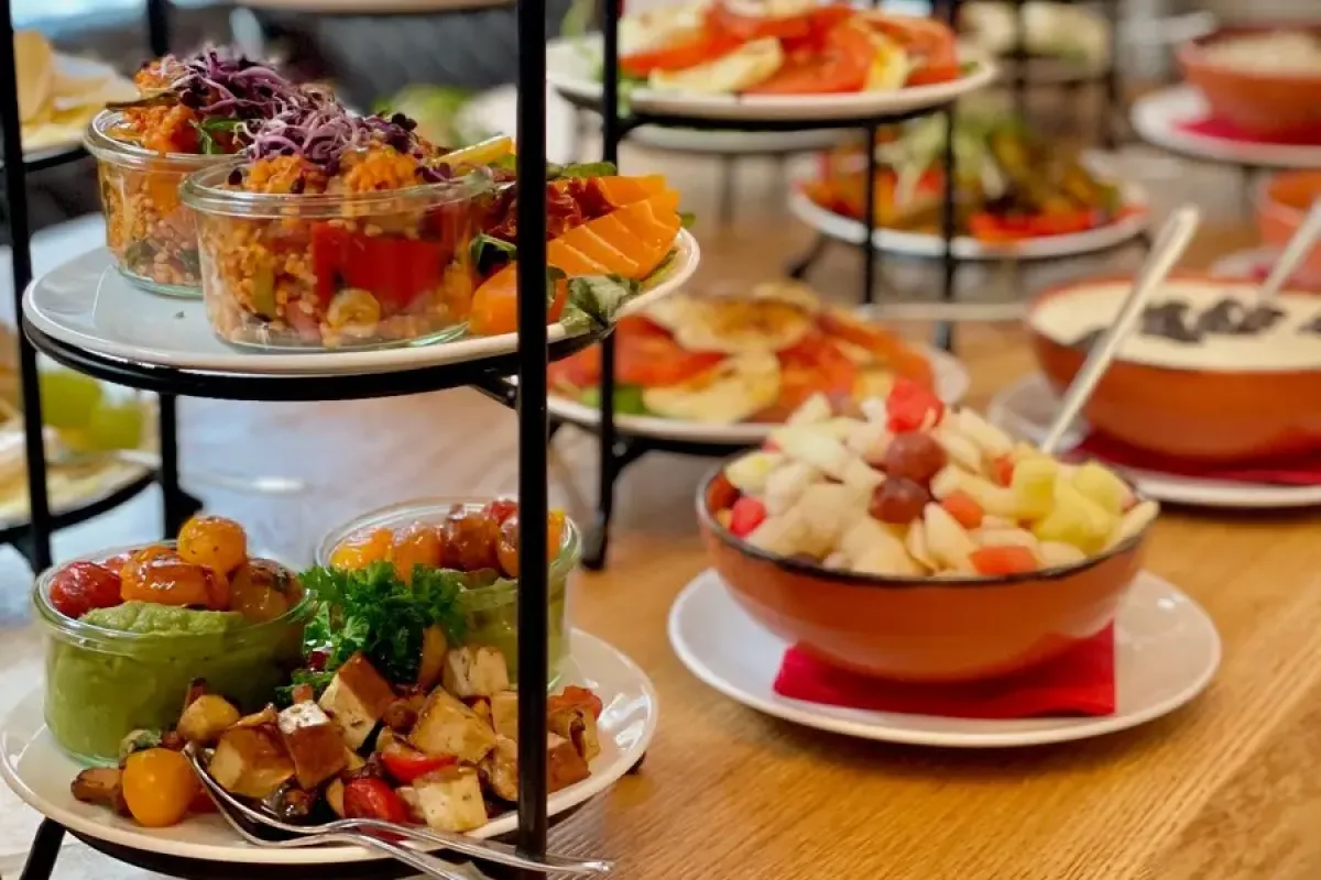 Etagere mit Salaten, Obst und Gemuese auf einem Fruehstuecksbuffet, dahinter belegte Platten und Schuesseln auf einem Holztisch