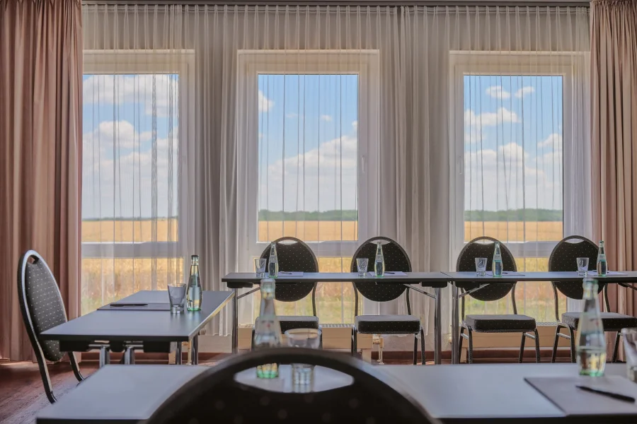Tagungsraum mit langer Tafel und dunklen St&uuml;hlen vor drei bodentiefen Fenstern mit Blick &uuml;ber Felder
