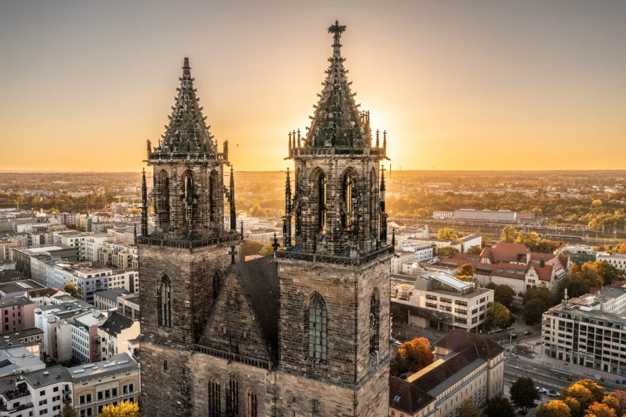 Die beiden Domtuerme aus der Luft im goldenen Abendlicht, dahinter die Daecher der Stadt bis zum Horizont