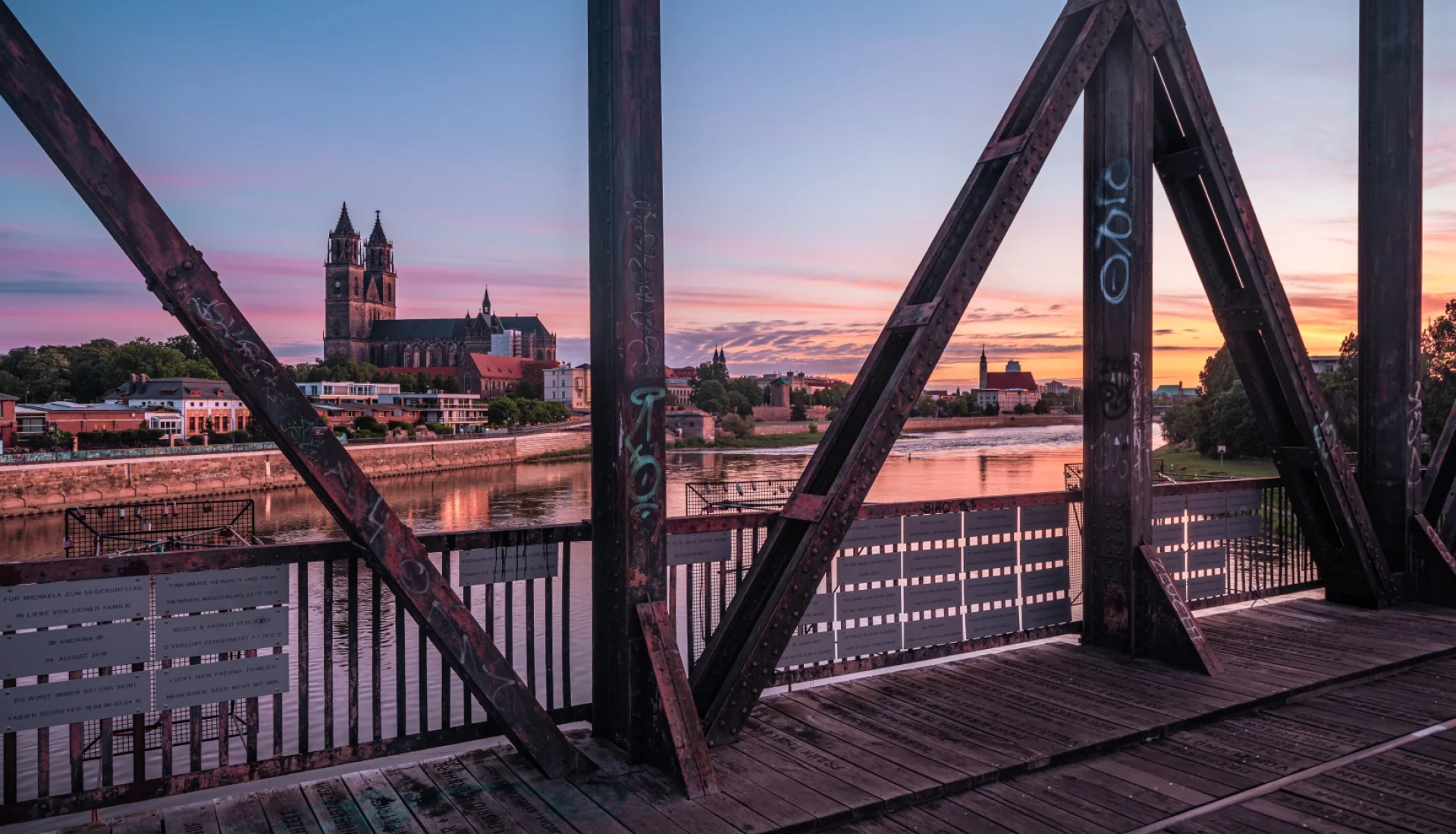 Blick durch das rostige Stahlfachwerk der Hubbr&uuml;cke auf den Magdeburger Dom, die Elbe leuchtet im rosa Abendrot