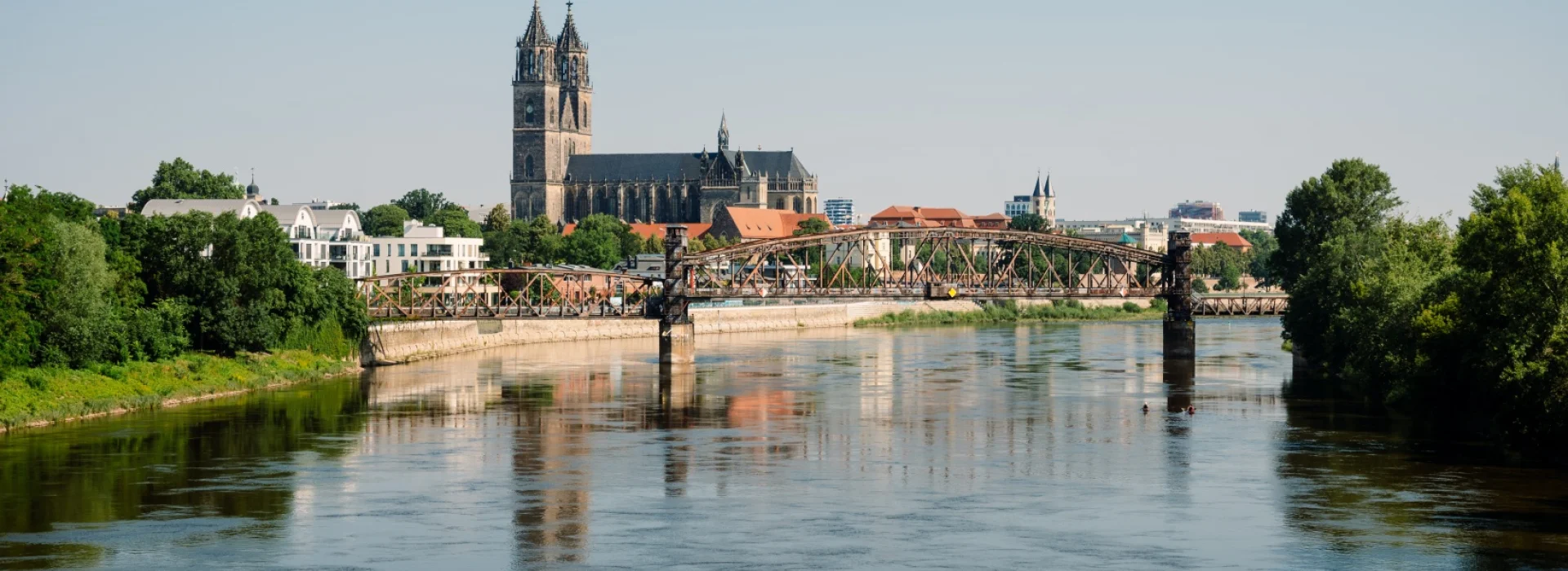 Blick ueber die Elbe auf den Magdeburger Dom, davor die historische Hubbruecke mit ihren eisernen Fachwerktraegern, gruene Ufer zu beiden Seiten