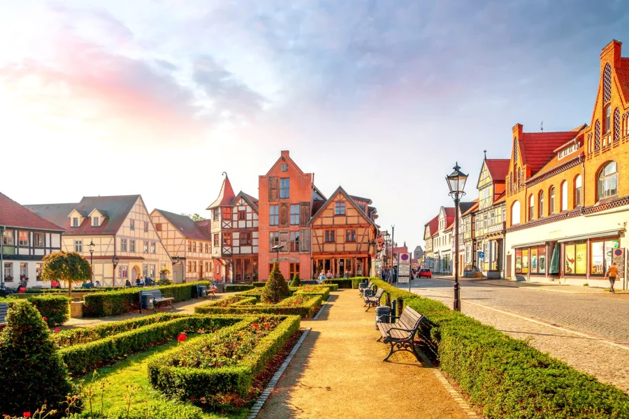 Sonnige Altstadt an der Elbe mit Fachwerk- und Backsteinhaeusern, vorn ein Platz mit Buchshecken, Rosenbeeten, Baenken und einer Gaslaterne