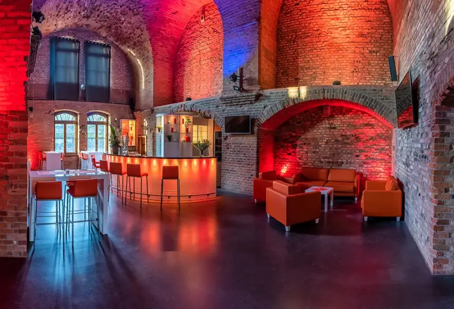 Bar im Backsteingew&ouml;lbe der Festung Mark mit rot-blauer Beleuchtung, geschwungenem Tresen, Barhockern und Ledersesseln
