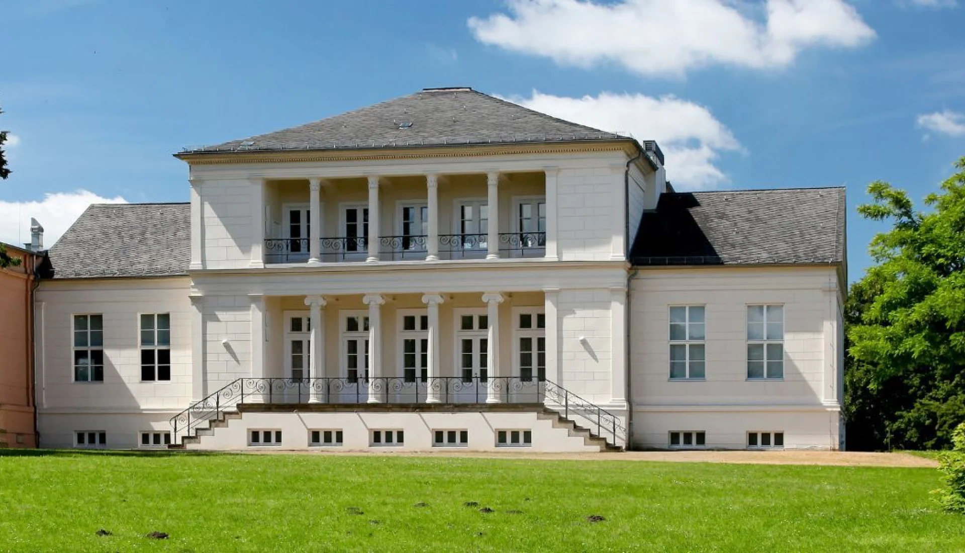 Wei&szlig;es Gesellschaftshaus Magdeburg frontal &uuml;ber einer Rasenfl&auml;che, mit S&auml;ulenloggia im Obergeschoss und geschwungener Freitreppe
