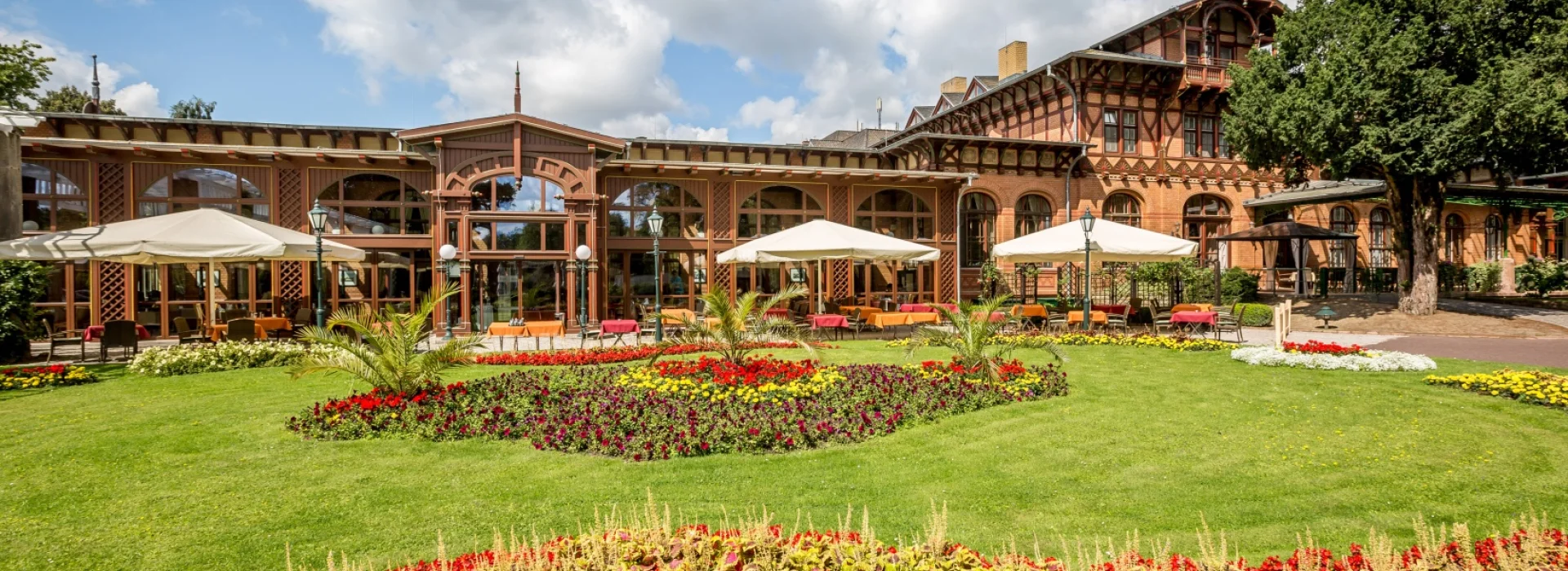 Dorint Herrenkrug Parkhotel: Jugendstilbau mit Fachwerk und verglastem Wintergarten, davor Terrasse mit wei&szlig;en Sonnenschirmen und leuchtend bepflanzte Blumenrabatten