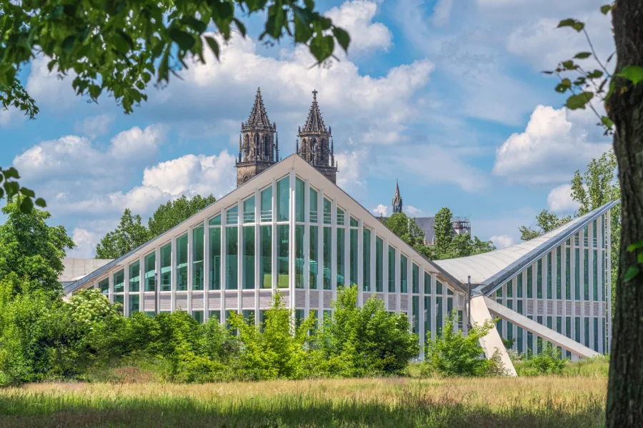 Die sanierte Hyparschale mit ihren geschwungenen Glasfassaden im Rotehornpark, dahinter die Tuerme des Magdeburger Doms