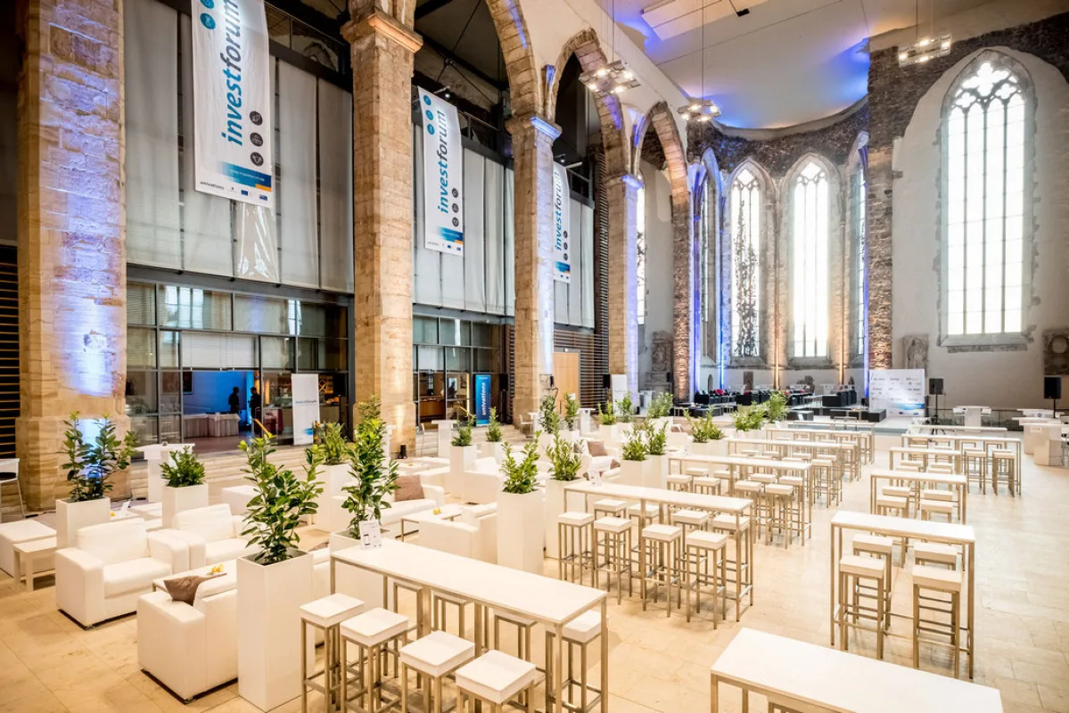 Empfang in der Johanniskirche mit weißen Stehtischen, Loungemöbeln und Veranstaltungsbannern zwischen den Sandsteinsäulen
