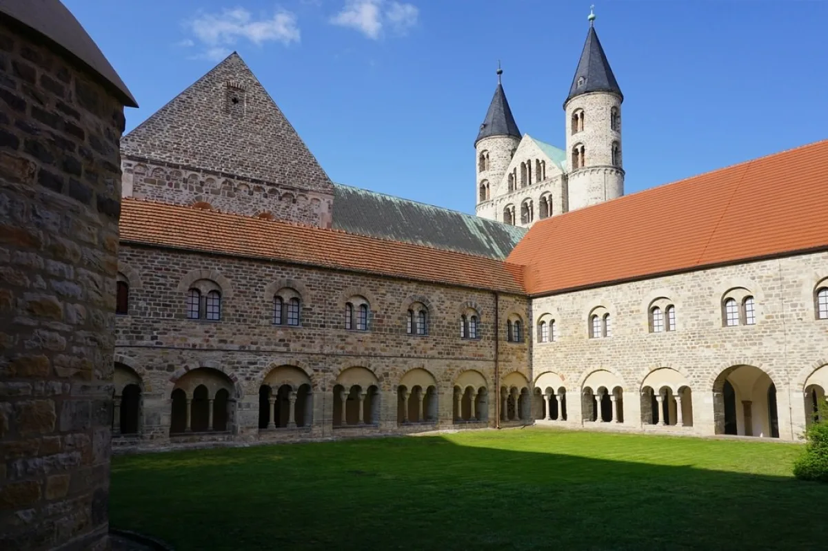 Sonniger Innenhof des Kreuzgangs im Kloster Unser Lieben Frauen mit Rasenfl&auml;che, romanischen S&auml;ulenarkaden und den Kircht&uuml;rmen im Hintergrund