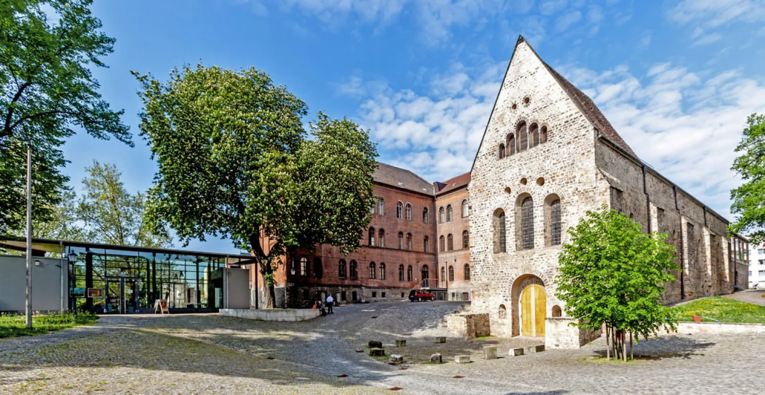 Gepflasterter Vorplatz des Klosters Unser Lieben Frauen mit gl&auml;sernem Infopavillon, rotem Backsteinbau und dem Westgiebel der Klosterkirche mit goldenem Portal
