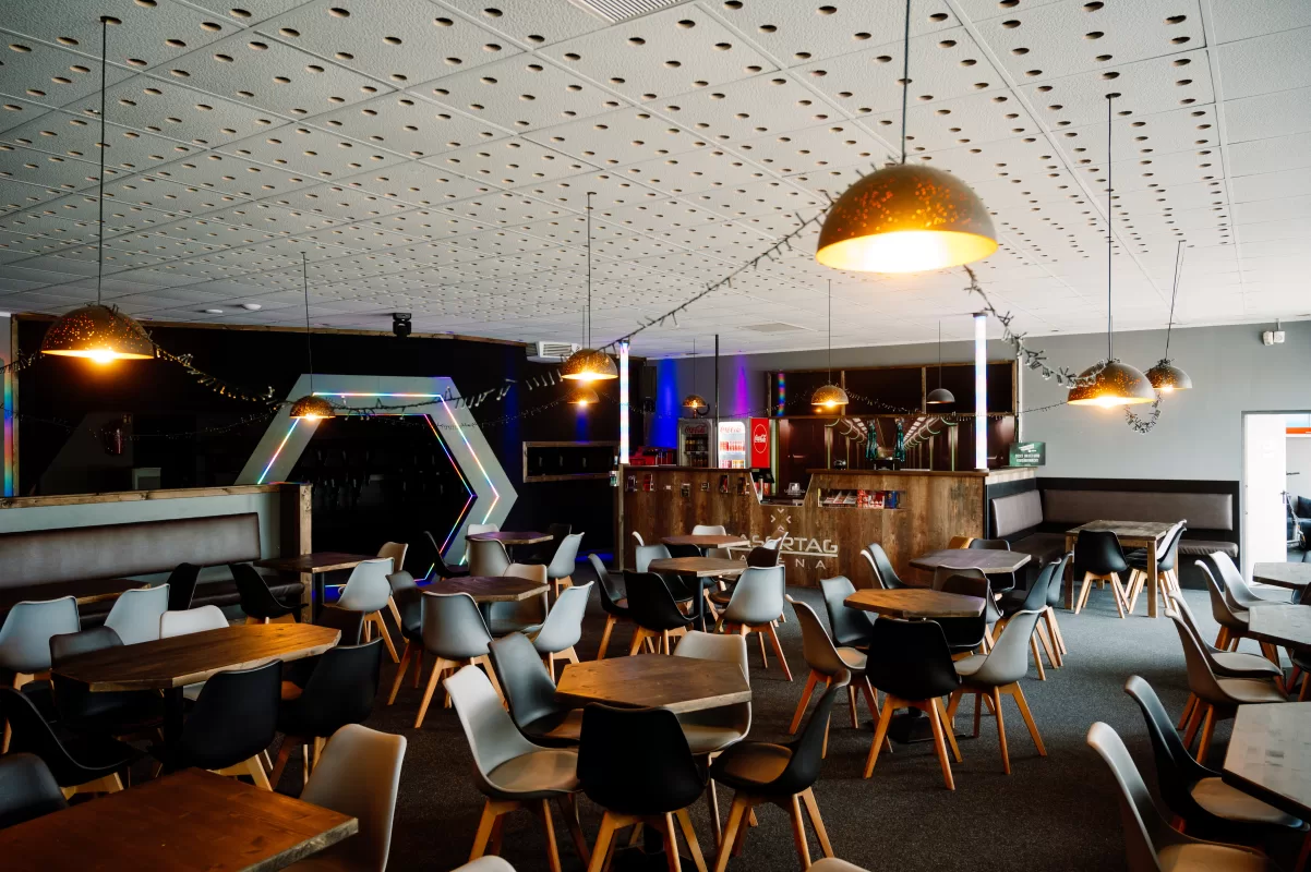 Aufenthaltsraum mit vielen Tischen und Stühlen in der Lasertag Arena Magdeburg mit einer Theke im HIntergrund.