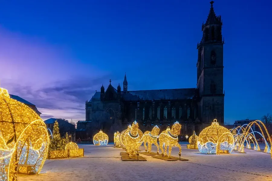 Lichterwelt auf dem Domplatz in der Abendd&auml;mmerung: riesige leuchtende Weihnachtskugeln und goldene Pferde aus Lichtpunkten vor der dunklen Silhouette des Doms