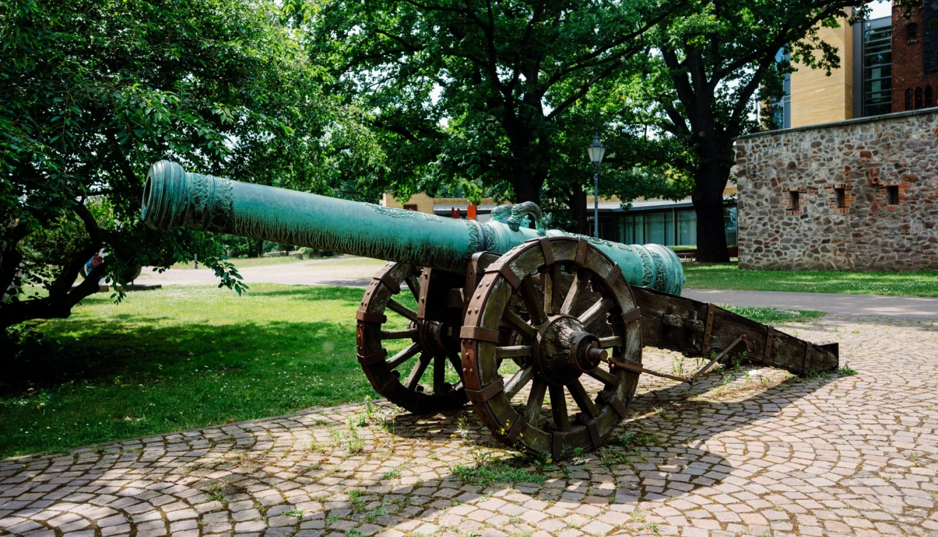 Historische Bronzekanone mit gr&uuml;ner Patina auf h&ouml;lzerner Lafette auf gepflastertem Grund vor der Stadtmauer an der Lukasklause