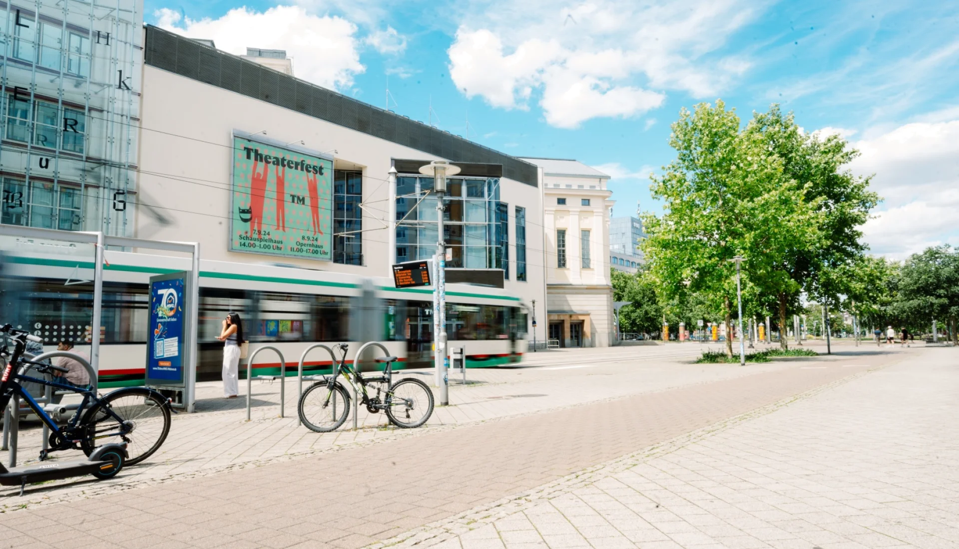 Stra&szlig;enbahn f&auml;hrt am Theater Magdeburg vorbei, an der Fassade h&auml;ngt ein gro&szlig;es Plakat f&uuml;r das Theaterfest