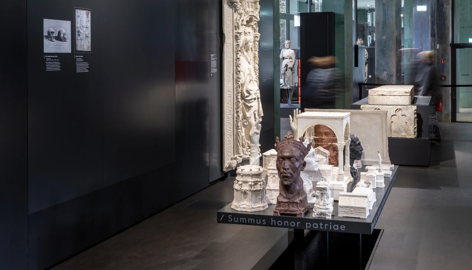 Ausstellungsraum im Dommuseum Ottonianum: Gipsmodelle und eine Bronzeb&uuml;ste auf einem langen Tisch vor dunklen W&auml;nden