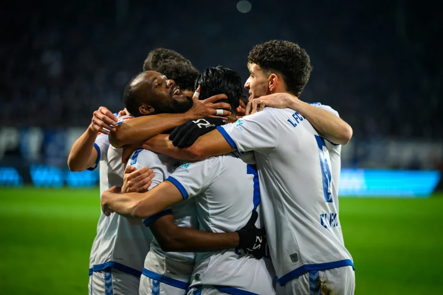 Jubeltraube des 1. FC Magdeburg: Spieler in weiss-blauen Trikots liegen sich nach einem Tor in den Armen, dahinter das dunkle Stadionrund im Flutlicht