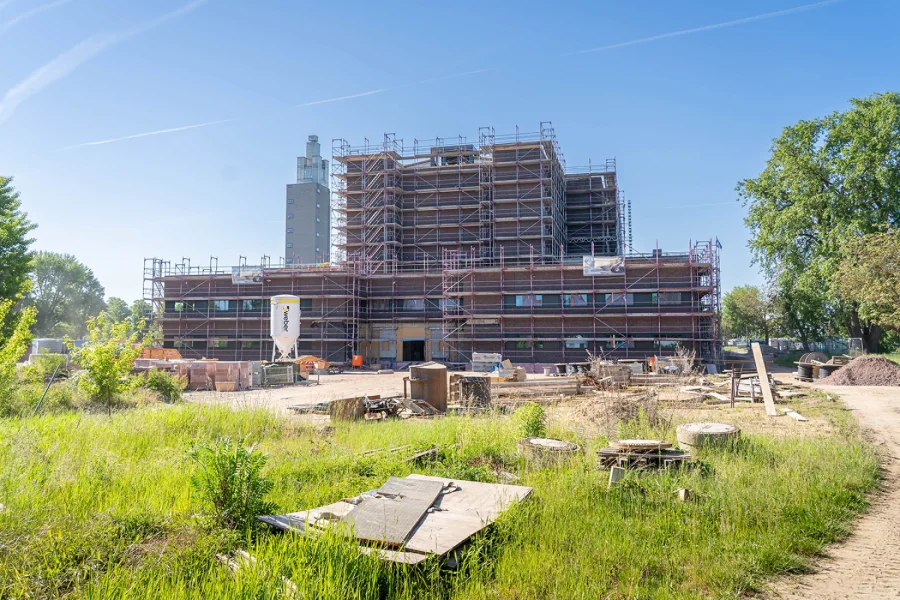 Die eingerueste Stadthalle Magdeburg waehrend der Sanierung: Backsteinbau mit Geruestlagen auf der Baustelle im Stadtpark, dahinter der Albinmueller-Turm