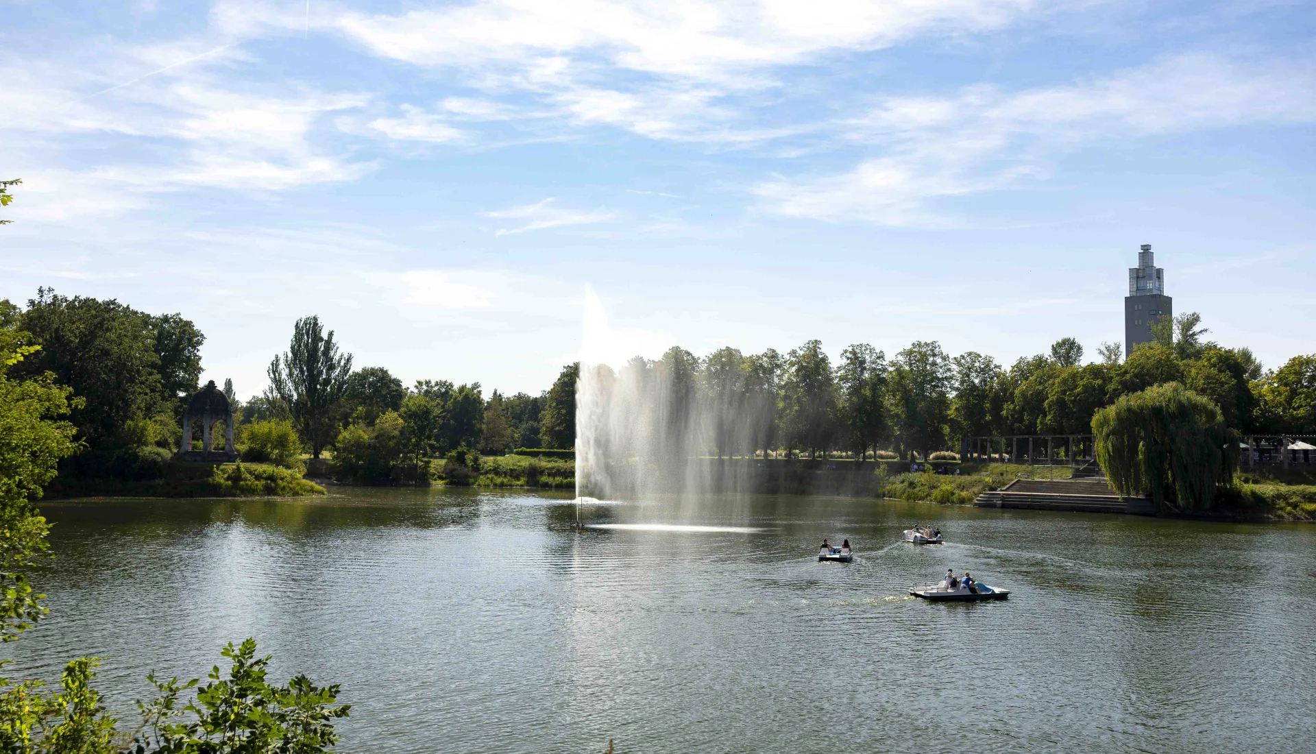 Blick auf den Adolf-Mittag-See mit Wasserfont&auml;ne und Tretbooten, im Hintergrund der Stadtpark mit Albinm&uuml;ller-Turm