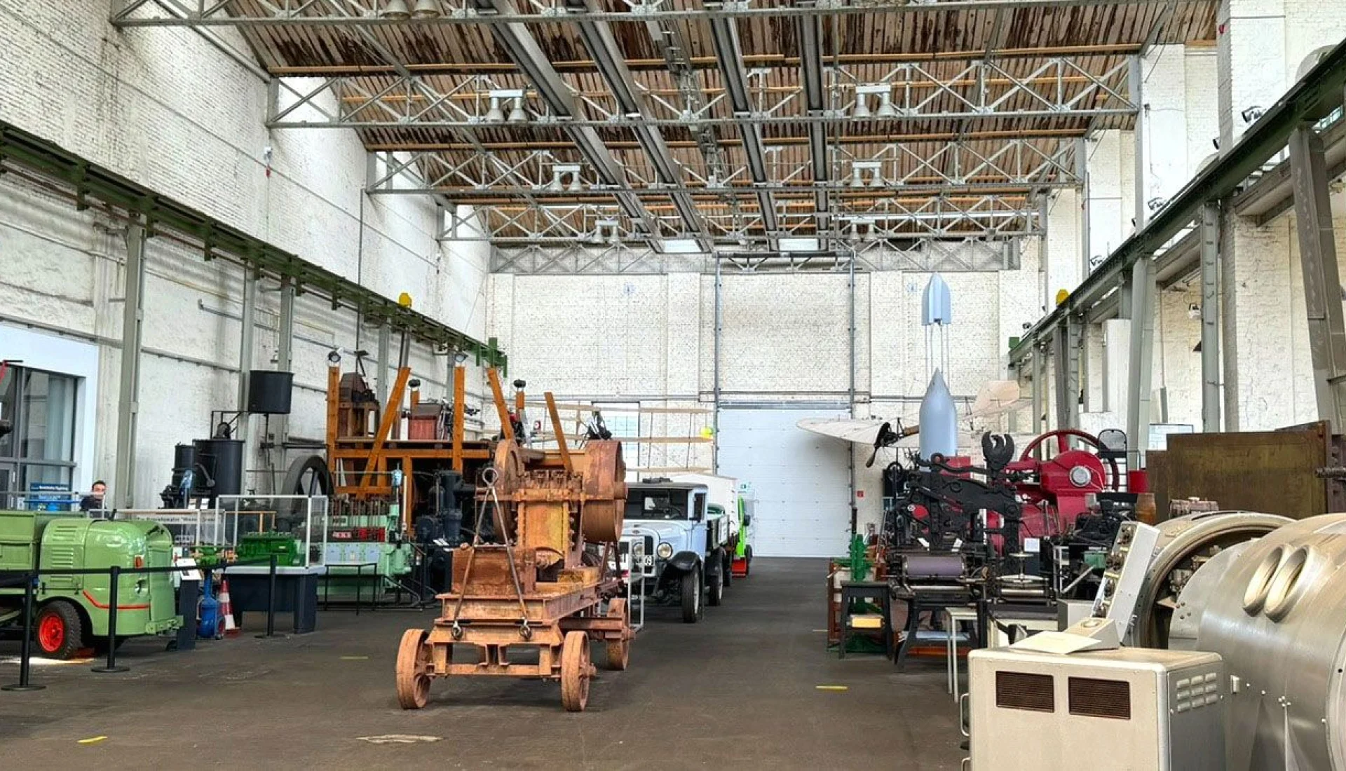 Weite Werkhalle des Technikmuseums mit historischen Maschinen, einem rostigen Bagger, Oldtimer-Lkw und Druckpressen unter offenem Dachstuhl