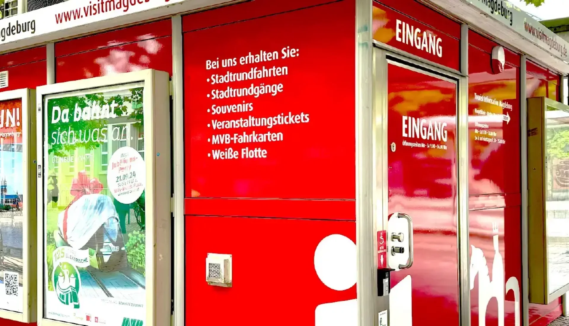Roter Verkaufspavillon der Tourist Information am Hauptbahnhof unter B&auml;umen, mit Eingangst&uuml;r, Plakaten und wei&szlig;em Stadtsilhouetten-Aufdruck