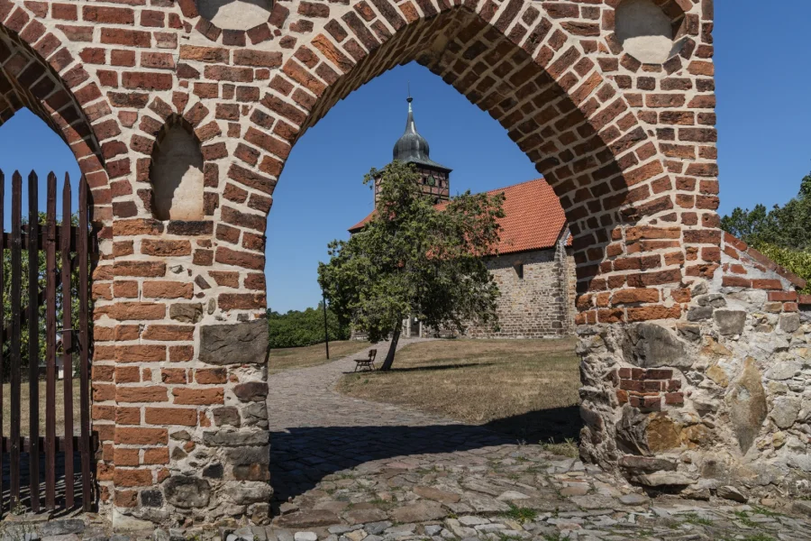 Die Dorfkirche St. Thomas in Pretzien, gesehen durch den Rundbogen des alten Friedhofstors