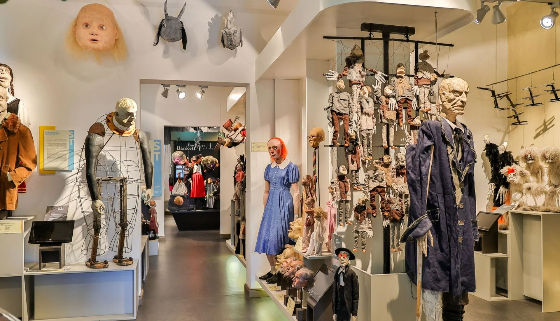Blick durch die Figurenspielsammlung in der villa p.: Figuren auf Sockeln, eine Wand voller h&auml;ngender Marionetten und eine Puppe im blauen Kleid
