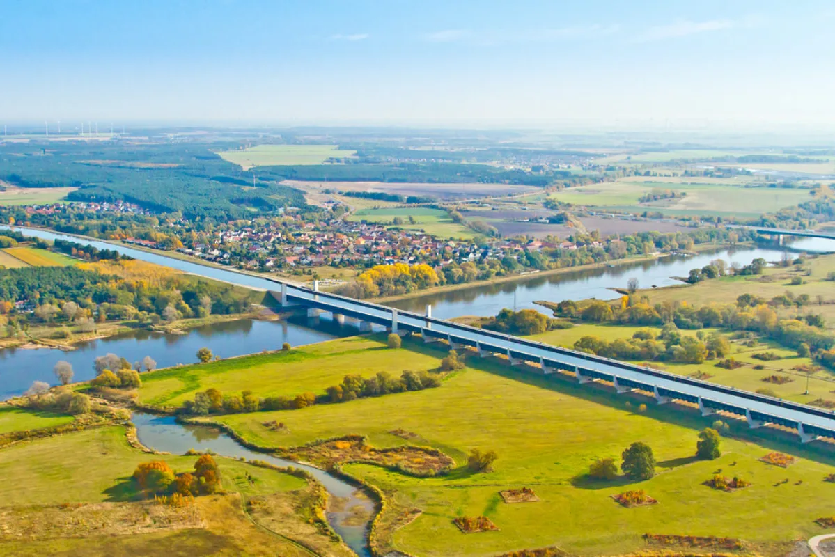 Weites Luftbild des Wasserstra&szlig;enkreuzes im Herbst: die lange Trogbr&uuml;cke quert die Elbe, dahinter Felder und ein Dorf