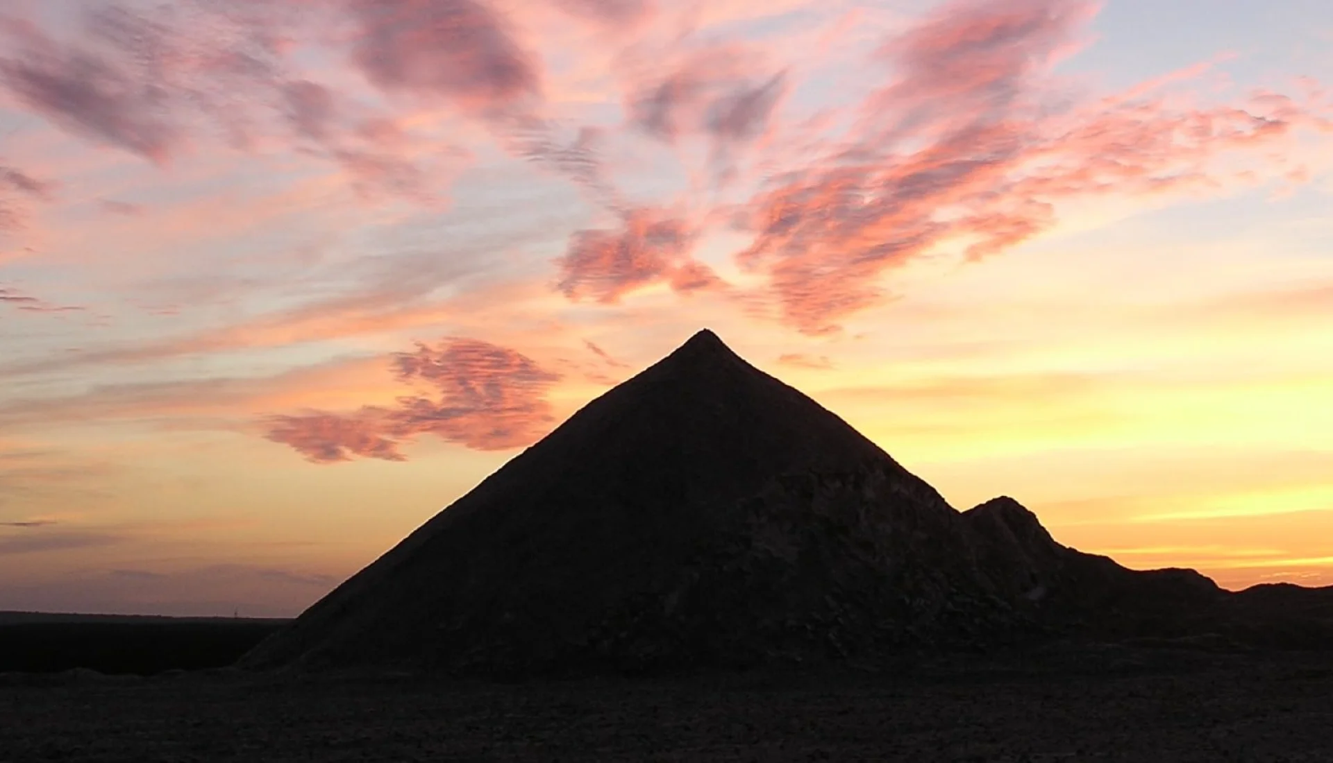 Die Halde des Kalimandscharo als dunkle Silhouette vor einem rosa und orange gef&auml;rbten Abendhimmel