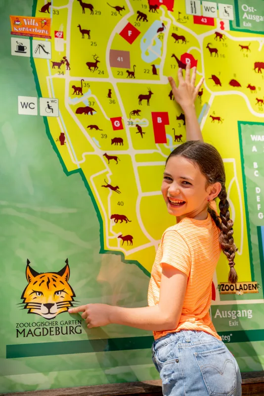 Mädchen zeigt lachend auf den Übersichtsplan des Zoologischen Gartens Magdeburg