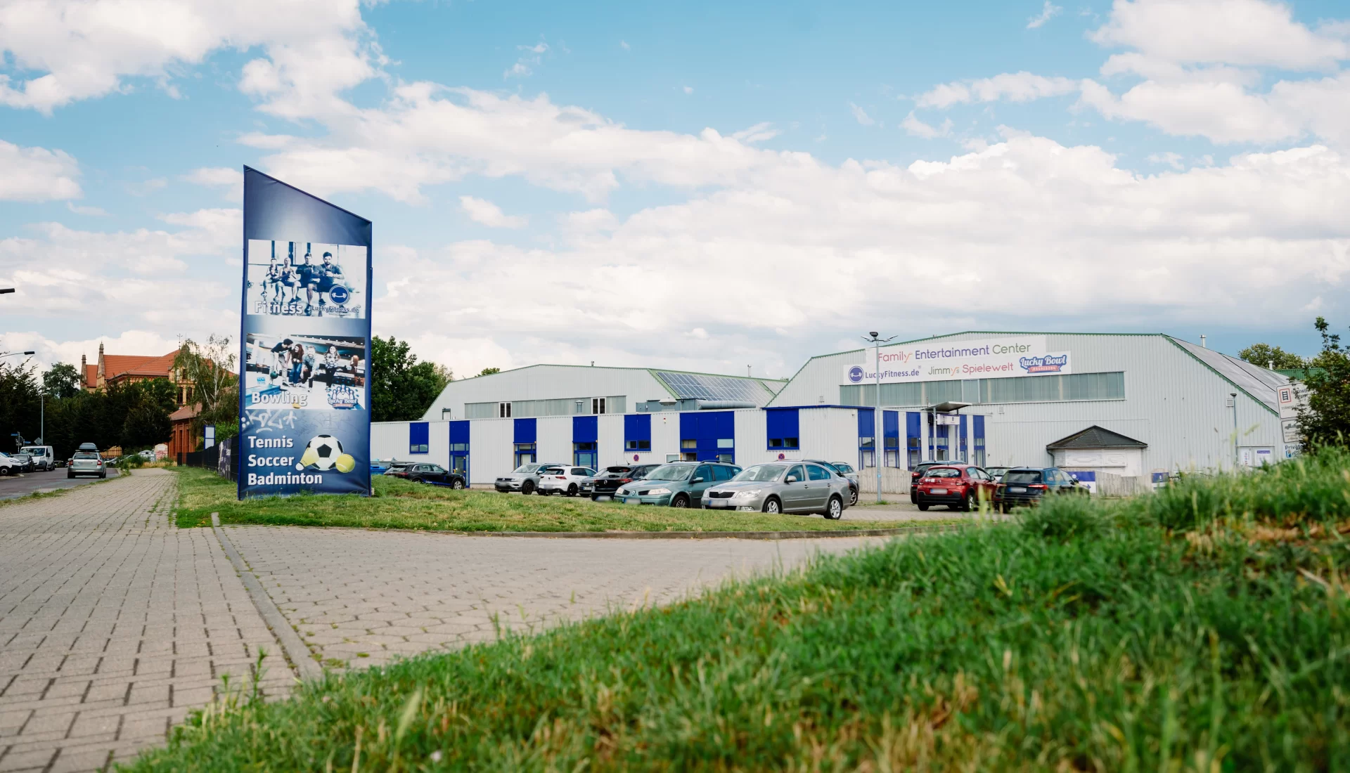 Au&szlig;enansicht der Lucky Fitness-Halle, davor Parkpl&auml;tze mit einigen Autos.