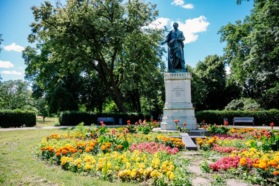 Blick auf eine Statue im Nordpark umgeben von gr&uuml;nen B&auml;umen und einem blauen Himmel. Im Vordergrund ein buntes Blumenbeet.