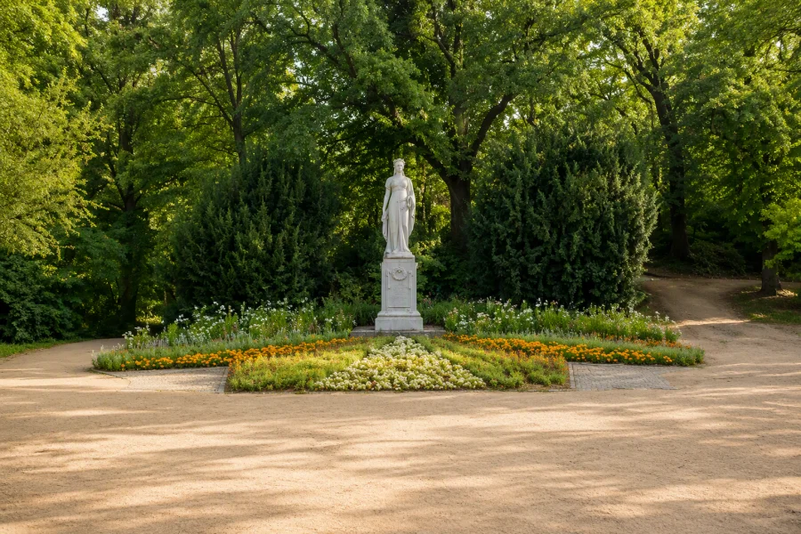 Blick auf das K&ouml;nig Luise Denkmal, umgeben von gr&uuml;nen B&auml;umen. Im Vordergrund des Denkmals ein bepflanztes Blumenbeet.