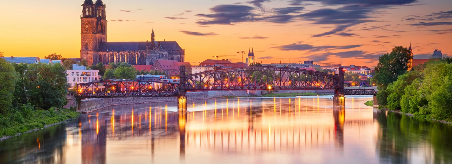 Abendrot ueber Magdeburg: Dom und alte Hubbruecke spiegeln sich mit ihren Lichtern in der ruhigen Elbe