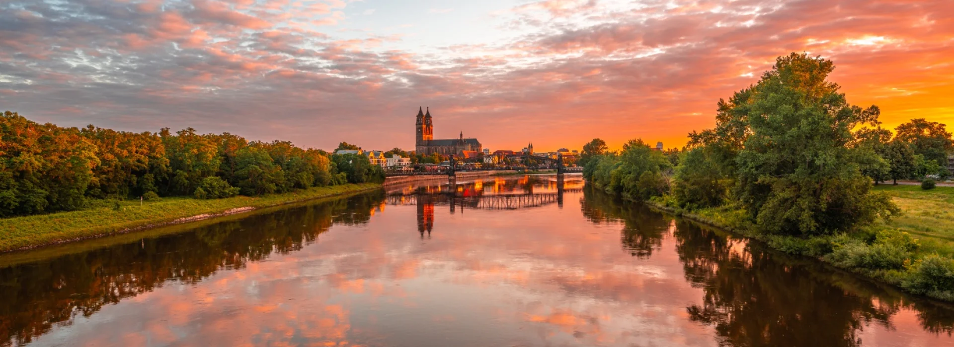 Sonnenaufgang ueber der Elbe: rosa Wolken spiegeln sich im Wasser, in der Mitte Dom und Hubbruecke am Horizont
