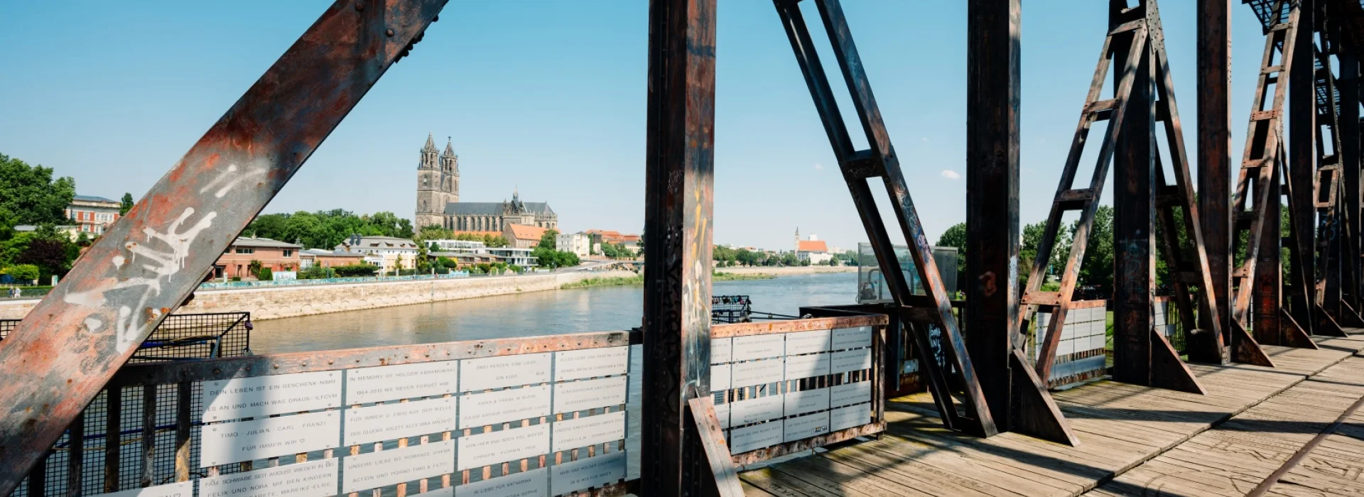 Blick durch die rostigen Stahltraeger der Hubbruecke mit Gedenktafeln am Gelaender, ueber die Elbe zum Magdeburger Dom