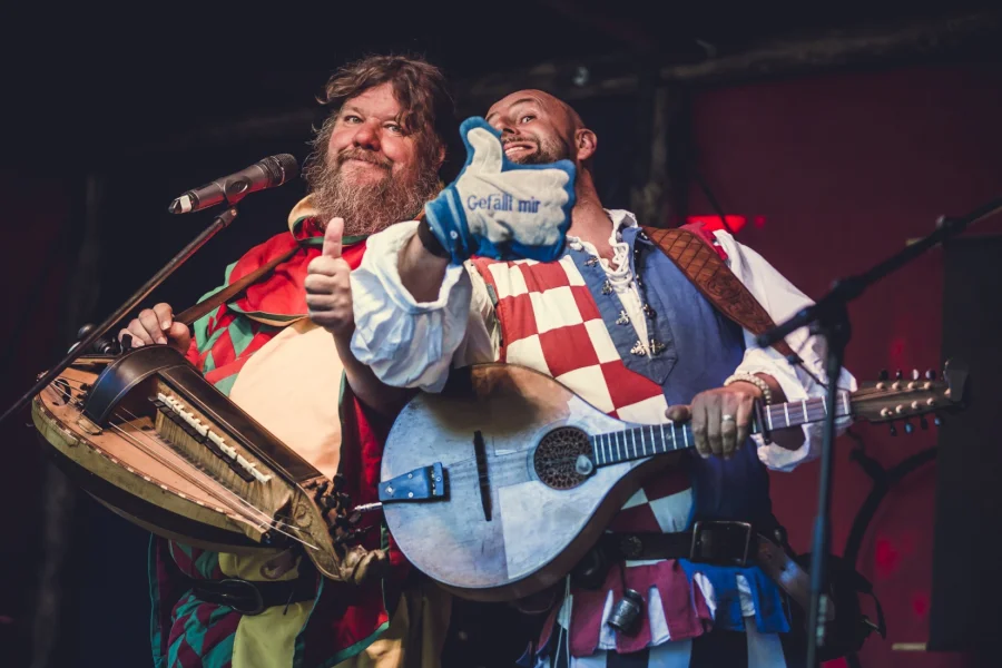 Zwei Musiker von Pampatutti auf der B&uuml;hne, einer mit Drehleier, der andere mit Mandola, dazu eine hochgehaltene Stoffhand mit der Aufschrift Gef&auml;llt mir